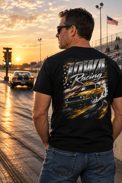 A man wearing a black graphic t-shirt with a yellow muscle car and 'Iowa Racing' text, standing on a racetrack at sunset.