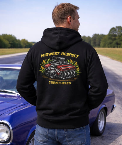 Person wearing a black hoodie with a graphic design and text, standing next to a classic car on a road.