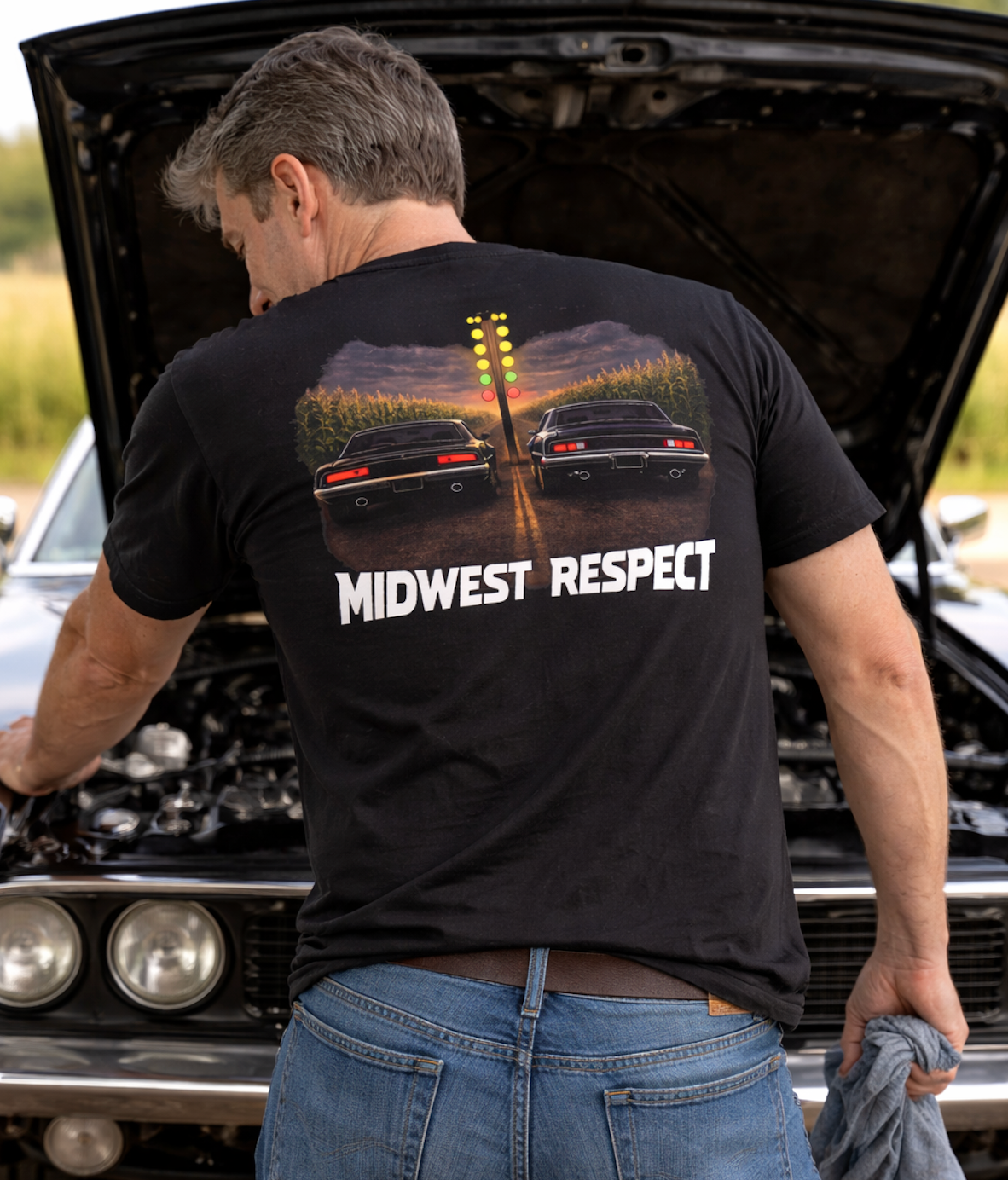 Man wearing a black 'Midwest Respect' t-shirt in front of an open car hood.