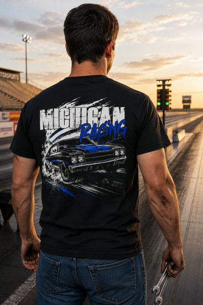A man viewed from behind wearing a black graphic t-shirt with a blue and white 'MICHIGAN RACING' design on the back, standing on a drag strip at sunset.