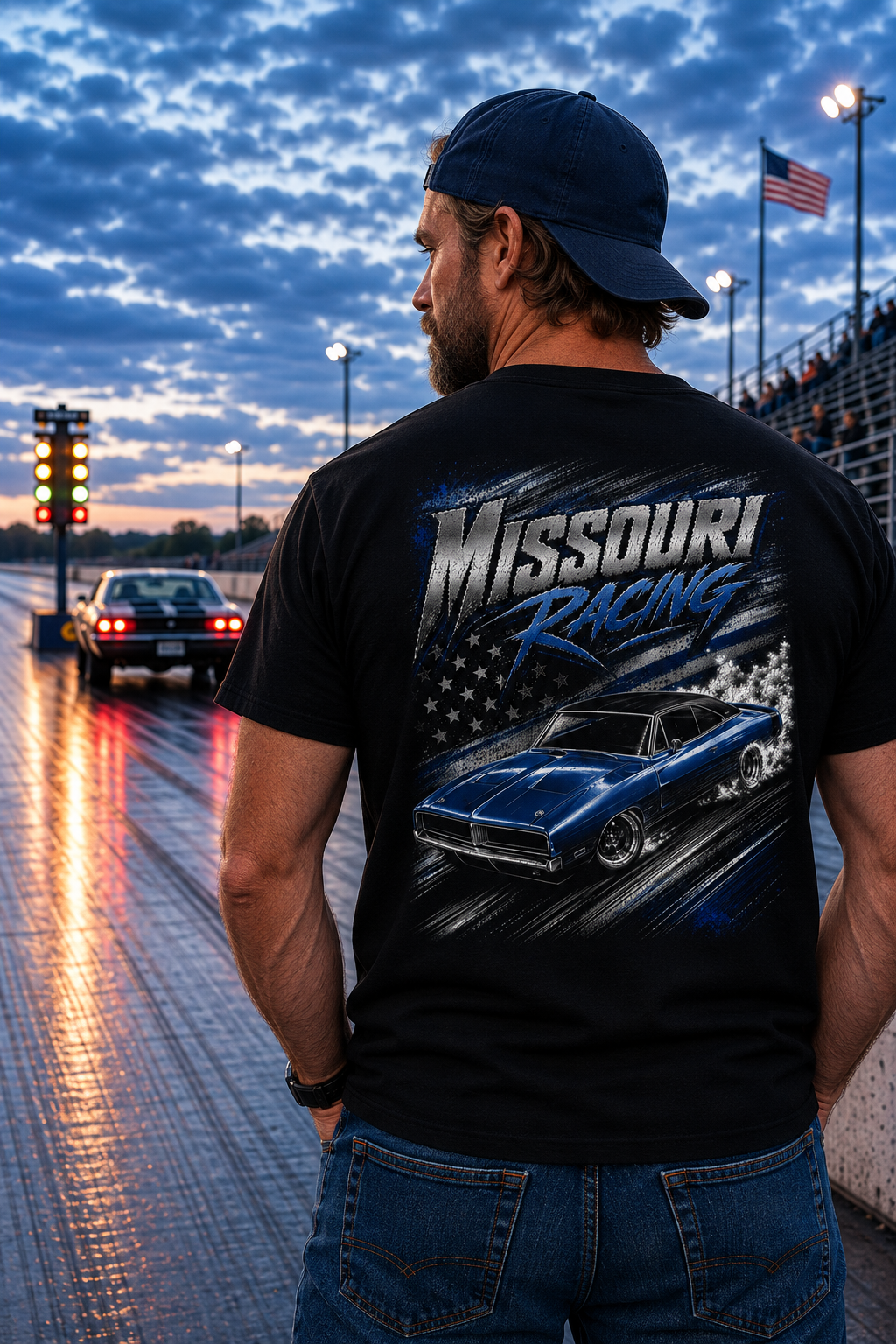 A man stands on a racetrack at dusk wearing a black t-shirt with a large 'Missouri Racing' graphic on the back, featuring a blue muscle car and American flag design.