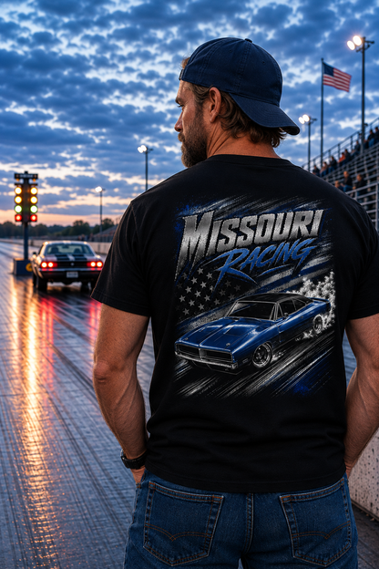 A man stands on a racetrack at dusk wearing a black t-shirt with a large 'Missouri Racing' graphic on the back, featuring a blue muscle car and American flag design.