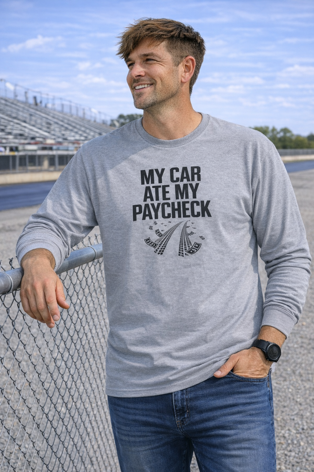 Man wearing a gray sweatshirt with text standing by a fence.