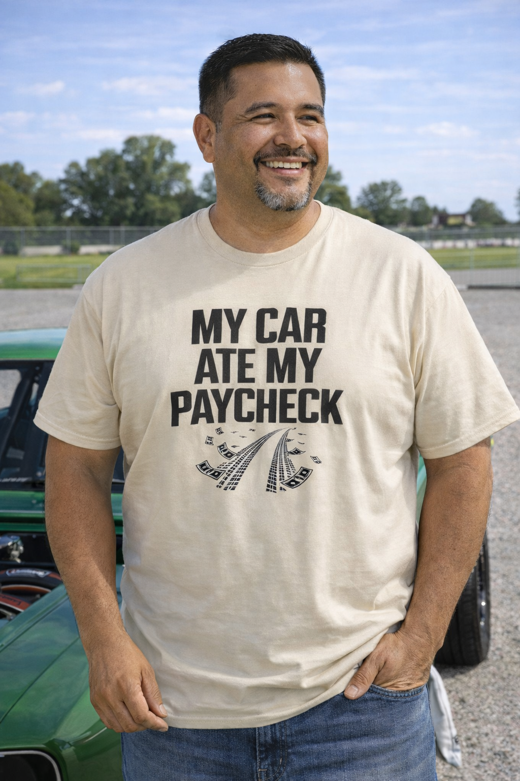 Man wearing a t-shirt with 'My car ate my paycheck' text standing next to a green car.