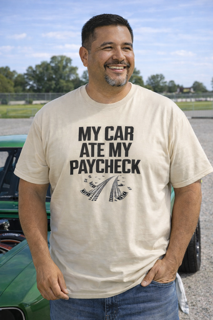 Man wearing a t-shirt with 'My car ate my paycheck' text standing next to a green car.