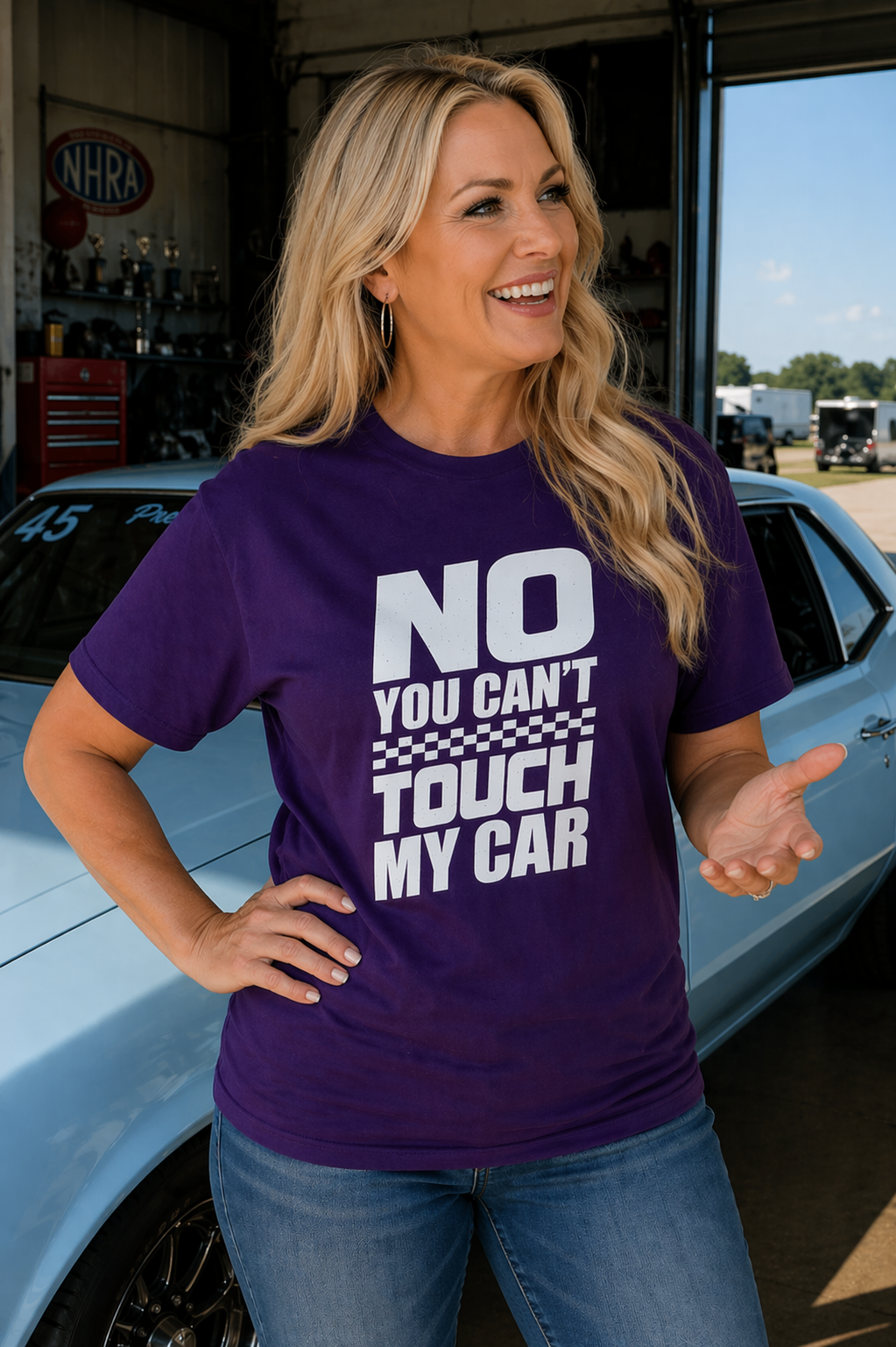Woman wearing a purple t-shirt with 'No You Can't Touch My Car' text, standing next to a car in a garage.