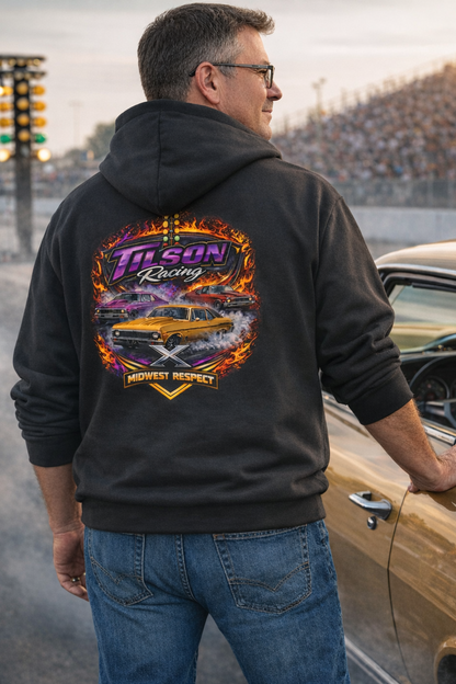 Man wearing a hoodie with 'Tilson Racing' design, standing next to a car on a racetrack.